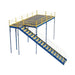 Stairway with yellow railing leading to a warehouse mezzanine, made of metal and bar grating, meeting IBC safety standards.
